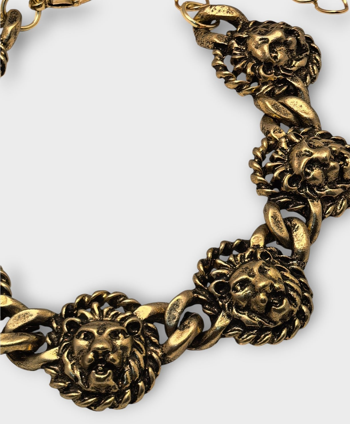 Gold chain necklace with lion head designs on a white background